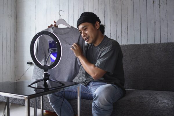 Influenceur vlogger en train de se filmer avec son smartphone, il montre un t-shirt, partenariat