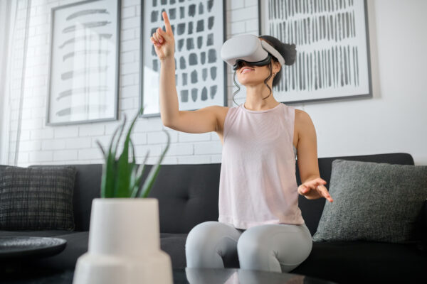 Réalité virtuelle, métaverse et gaming avec une femme dans le salon de sa maison utilisant un casque.